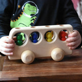 Close up of a child playing with the Ostheimer Natural Bus With 4 People. The child is pushing thew bus along a wooden surface.
