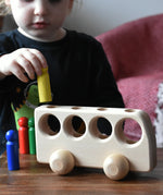 Close up of a child playing with the Ostheimer Natural Bus With 4 People. The child is placing the yellow coloured figure into one of the slots on the top of the bus.