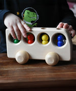 Close up of a child playing with the Ostheimer Natural Bus With 4 People. The child is pushing thew bus along a wooden surface.