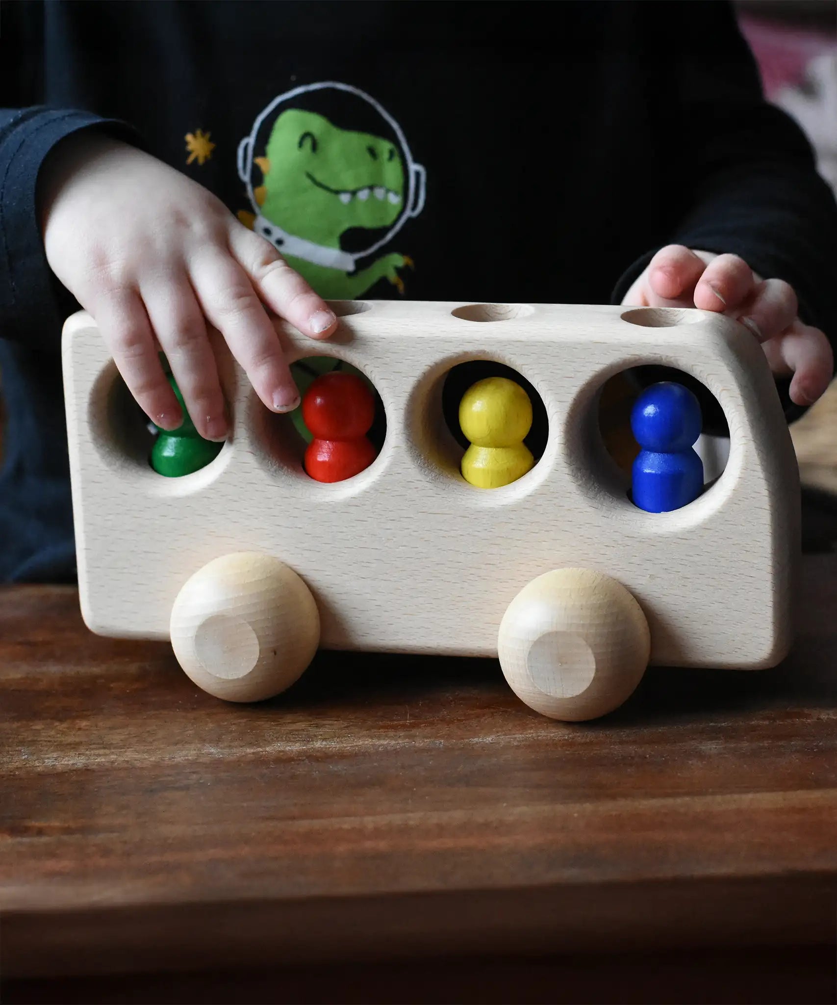 Close up of a child playing with the Ostheimer Natural Bus With 4 People. The child is pushing thew bus along a wooden surface.