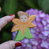 An Ostheimer hand made and hand painted wooden Calendula Flower Child figure toy shown in an adult's hand for scale. These flower child wooden figures are part of a wide range of expertly hand crafted wooden toys here at Babipur. 
