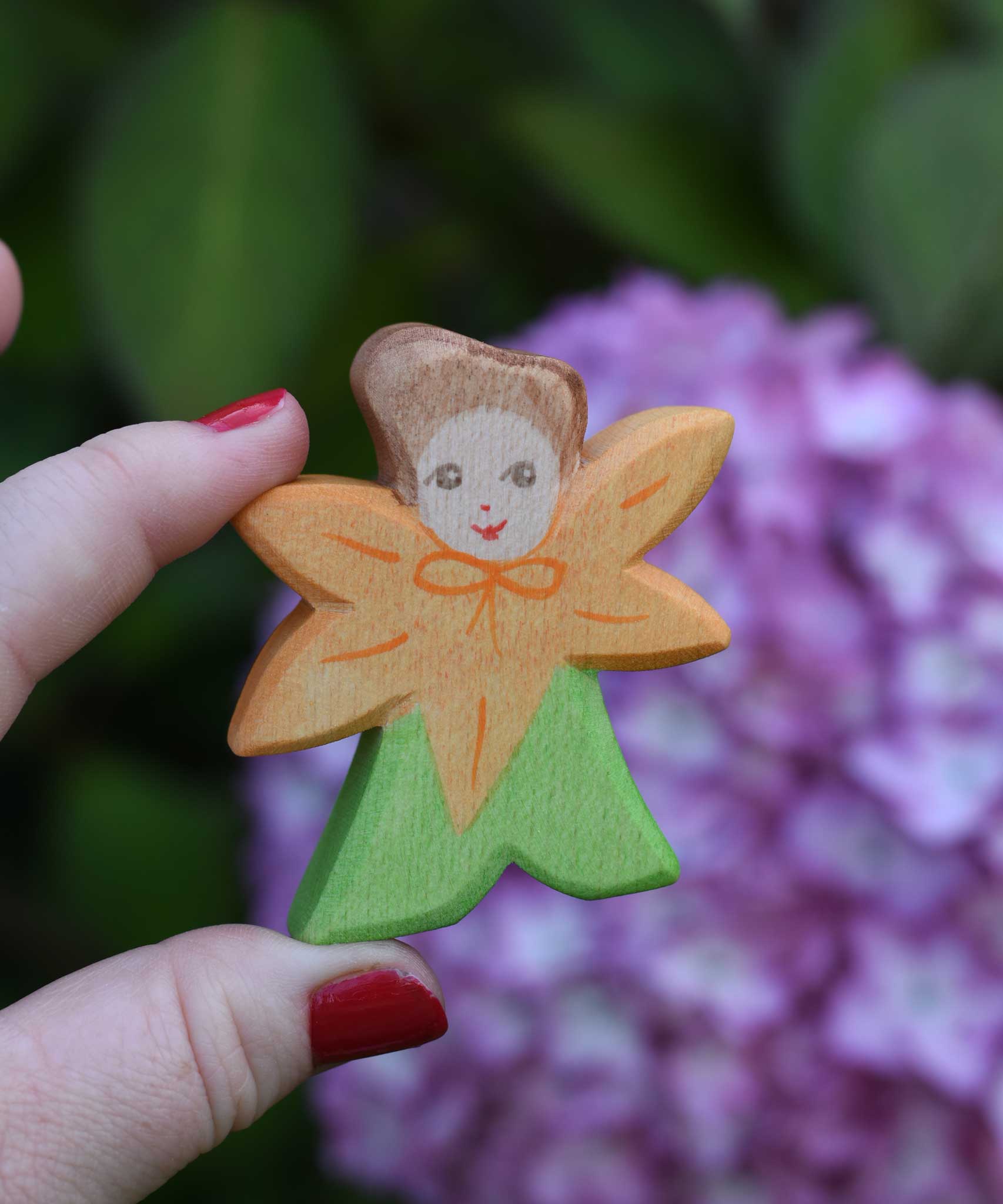 An Ostheimer hand made and hand painted wooden Calendula Flower Child figure toy shown in an adult's hand for scale. These flower child wooden figures are part of a wide range of expertly hand crafted wooden toys here at Babipur. 