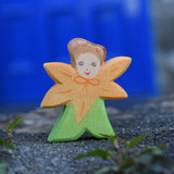 An Ostheimer hand made and hand painted wooden Calendula Flower Child figure toy placed on a stone wall outdoors. These flower child wooden figures are part of a wide range of expertly hand crafted wooden toys here at Babipur. 