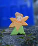 An Ostheimer hand made and hand painted wooden Calendula Flower Child figure toy placed on a stone wall outdoors. These flower child wooden figures are part of a wide range of expertly hand crafted wooden toys here at Babipur. 