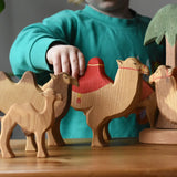 Child playing with a collection of Ostheimer handmade camel wooden toy figures.