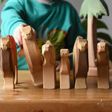 Six Ostheimer camel wooden toy figures lined up with a child holding one of them. Tall palm tree in the background.
