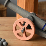 Ostheimer cannon wooden toy with 10 wooden balls placed on a wooden surface. Close up of the brown wheel.