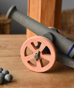 Ostheimer cannon wooden toy with 10 wooden balls placed on a wooden surface. Close up of the brown wheel.