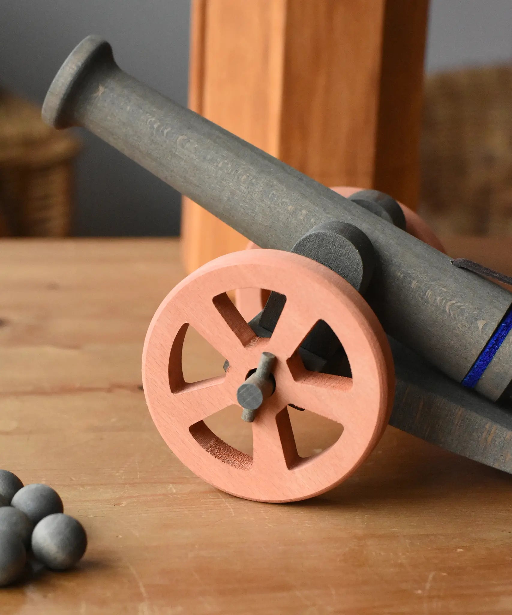 Ostheimer cannon wooden toy with 10 wooden balls placed on a wooden surface. Close up of the brown wheel.