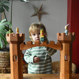 Ostheimer wooden castle bridge toy placed inbetween two round towers with princesses, frog king and dragon figures placed on the towers.
