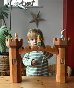 Ostheimer wooden castle bridge toy placed inbetween two round towers with princesses, frog king and dragon figures placed on the towers.