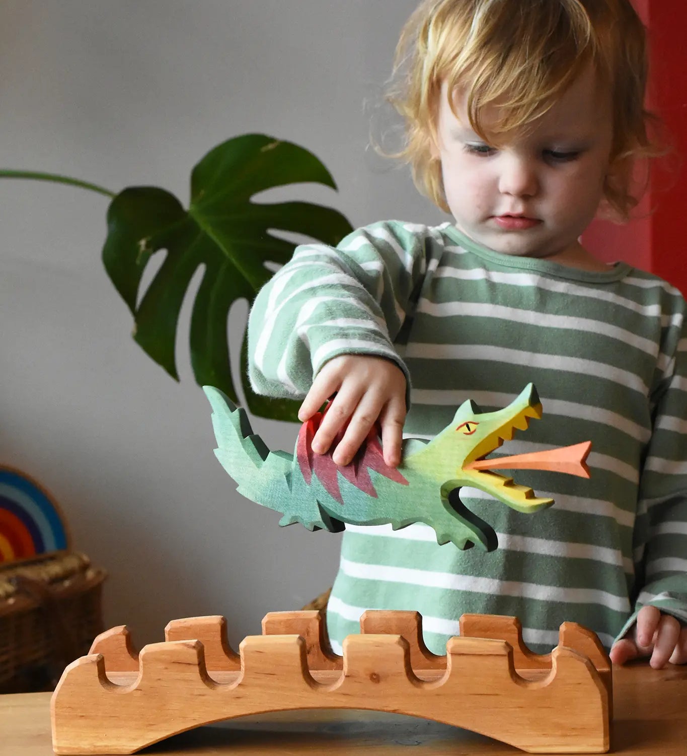 Ostheimer wooden castle bridge toy with a child placing a green dragon on it. 