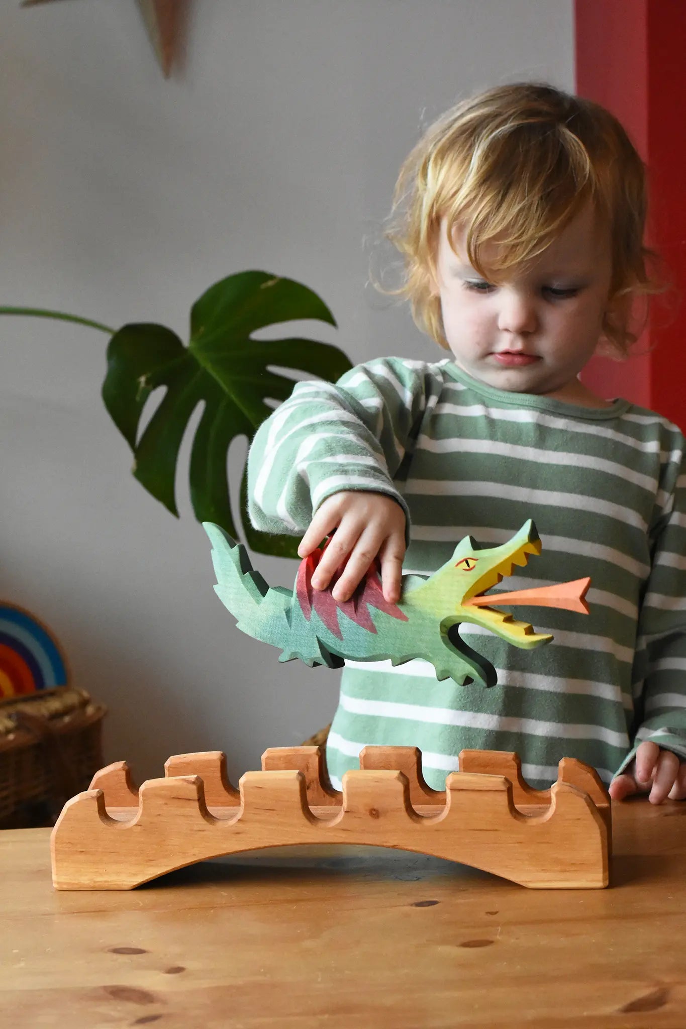 Ostheimer wooden castle bridge toy with a child placing a green dragon on it. 