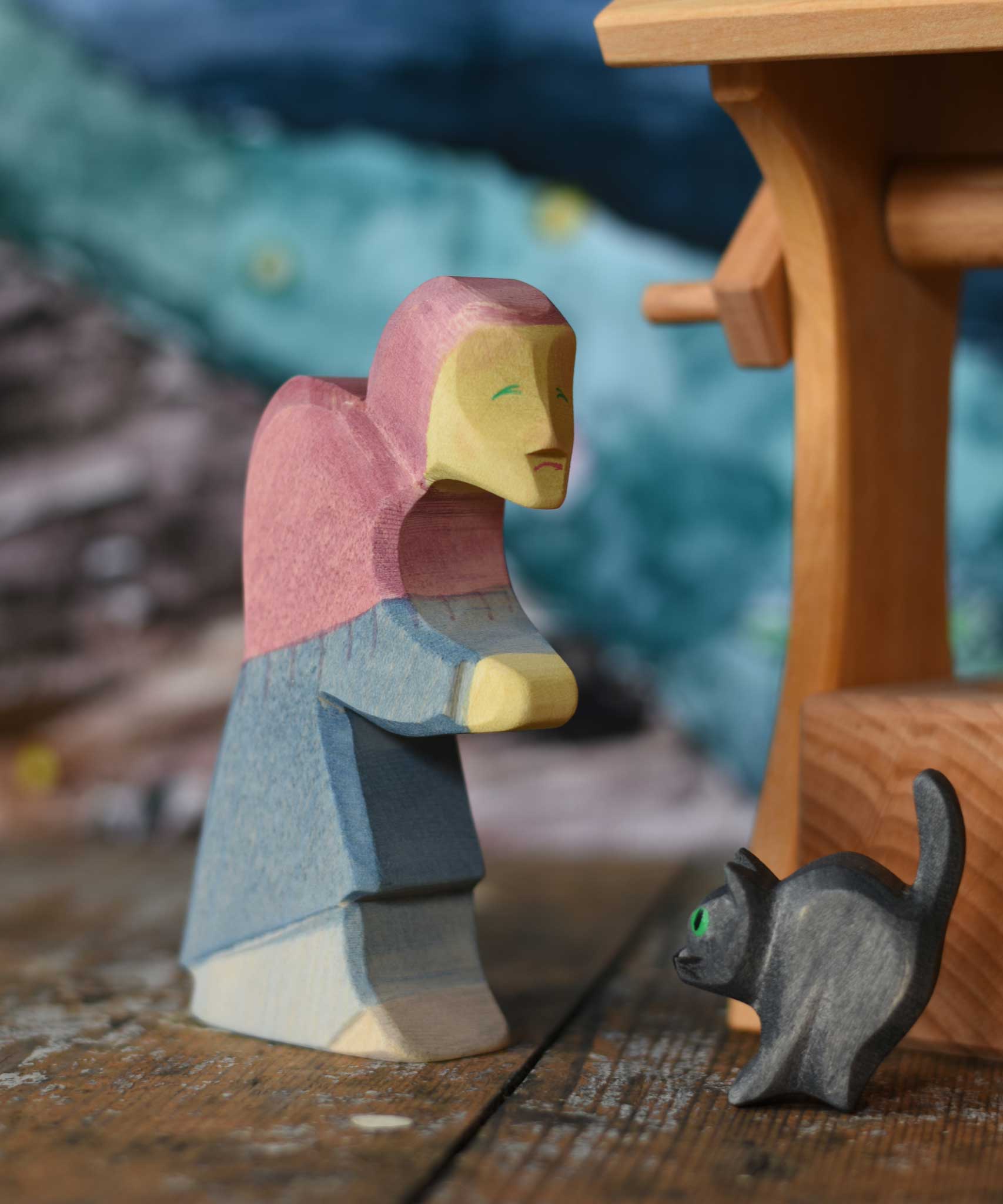 Ostheimer hand made and hand painted wooden witch and cat figures  placed on a wooden surface. An Ostheimer wooden well can be seen in the background. These wooden figures are part of a wide range of expertly hand crafted wooden toys here at Babipur. 