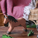 Ostheimer brown cold blood horse wooden toy figure placed in a simple small world play scene with wooden green grass scenery pieces. 