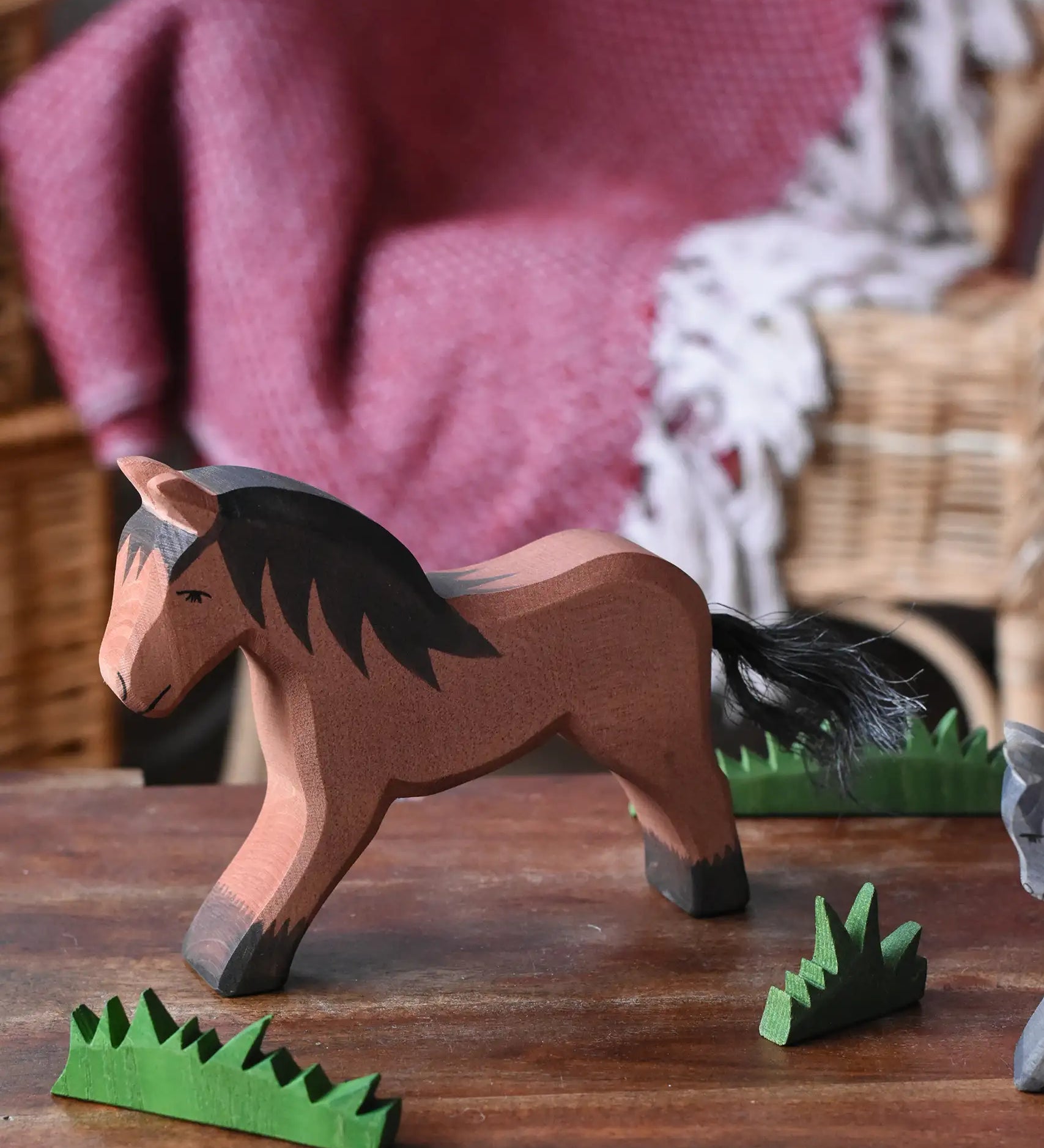 Ostheimer brown cold blood horse wooden toy figure placed in a simple small world play scene with wooden green grass scenery pieces. 