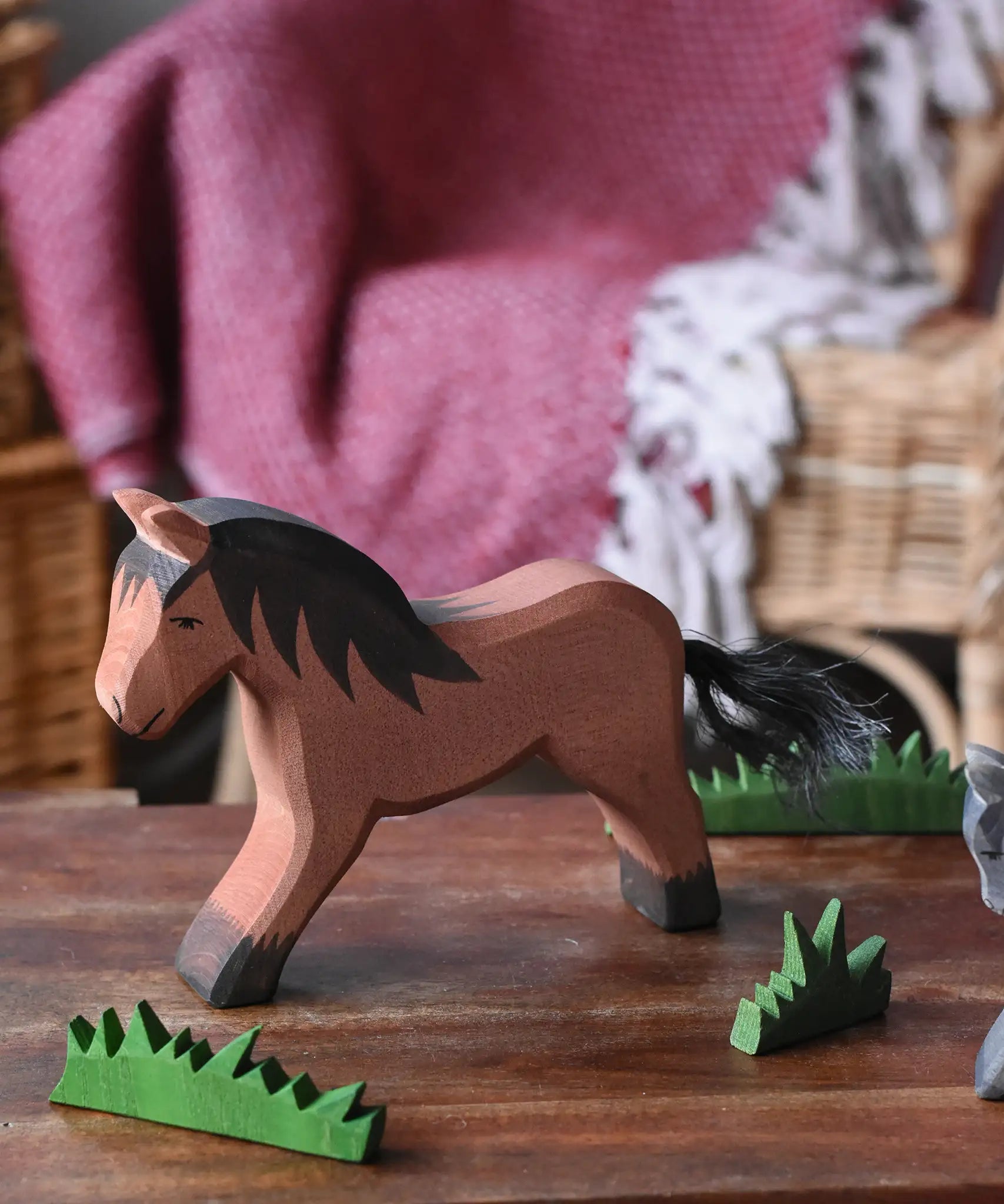 Ostheimer brown cold blood horse wooden toy figure placed in a simple small world play scene with wooden green grass scenery pieces. 