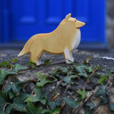 An Ostheimer Collie Dog Handmade Wooden Toy placed on a stone wall outdoors. These wooden figures are part of a large range of expertly hand crafted, Waldorf inspired, wooden toys here at Babipur.