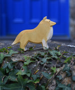 An Ostheimer Collie Dog Handmade Wooden Toy placed on a stone wall outdoors. These wooden figures are part of a large range of expertly hand crafted, Waldorf inspired, wooden toys here at Babipur.