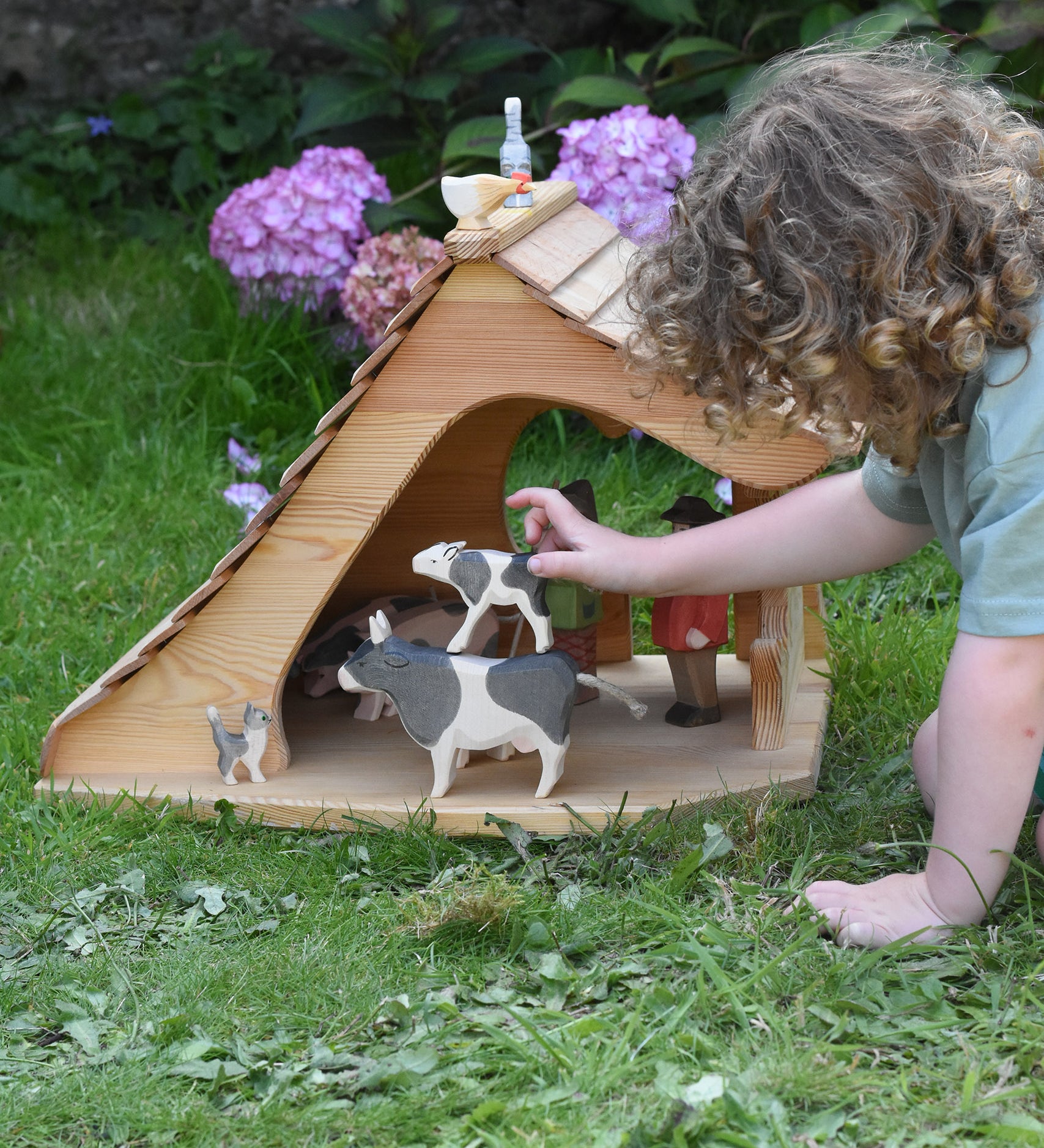 A child placing an Ostheimer drinking calf on a black and white standing cow figure in the Ostheimer cottage. These wooden figures are part of a large range of expertly hand crafted, Waldorf inspired, wooden toys here at Babipur. 