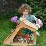 An Ostheimer wooden cottage dolls house filled with various Ostheimer animal and people figures. A child is holding a wooden cow figure, walking it across the roof of the cottage. 
These wooden figures are part of a large range of expertly hand crafted, Waldorf inspired, wooden toys here at Babipur. 