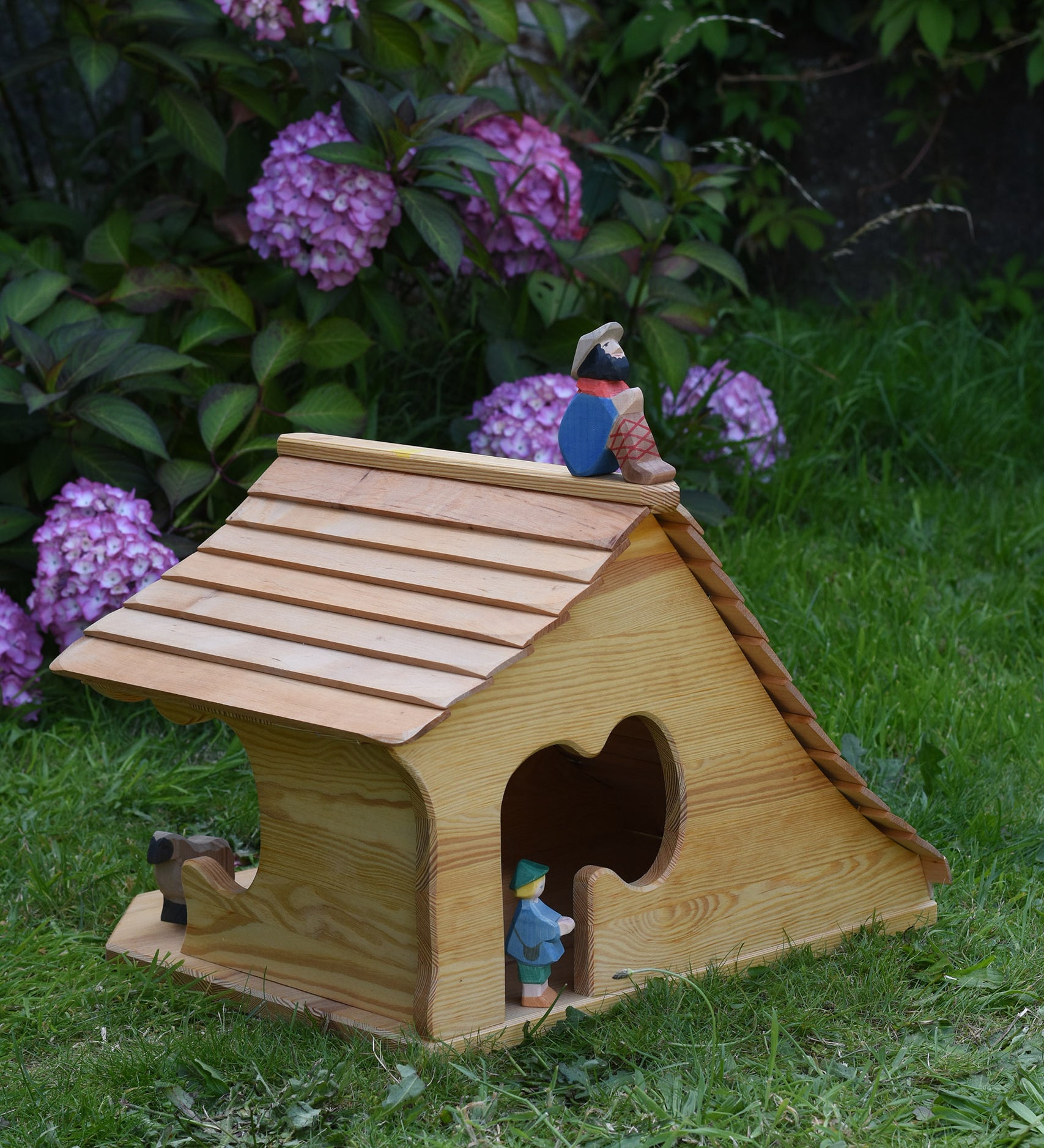 An Ostheimer wooden cottage dolls house with an sitting shepard figure placed on the roof. These wooden figures are part of a large range of expertly hand crafted, Waldorf inspired, wooden toys here at Babipur. 
