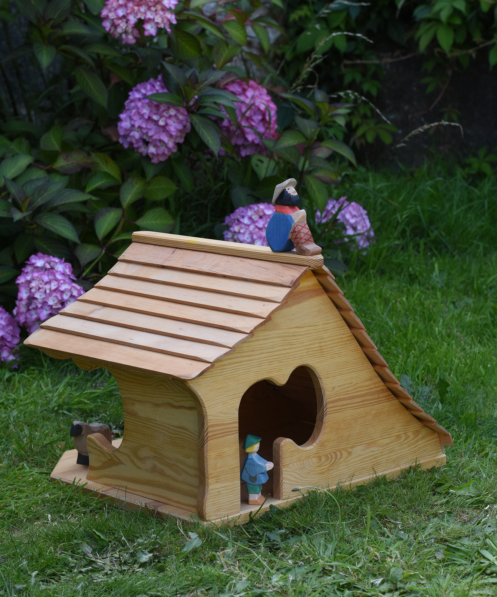 An Ostheimer wooden cottage dolls house with an sitting shepard figure placed on the roof. These wooden figures are part of a large range of expertly hand crafted, Waldorf inspired, wooden toys here at Babipur. 