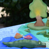 Ostheimer crocodile wooden toy figure placed on a blue Laura's cotton play cloth in a small world play scene. 