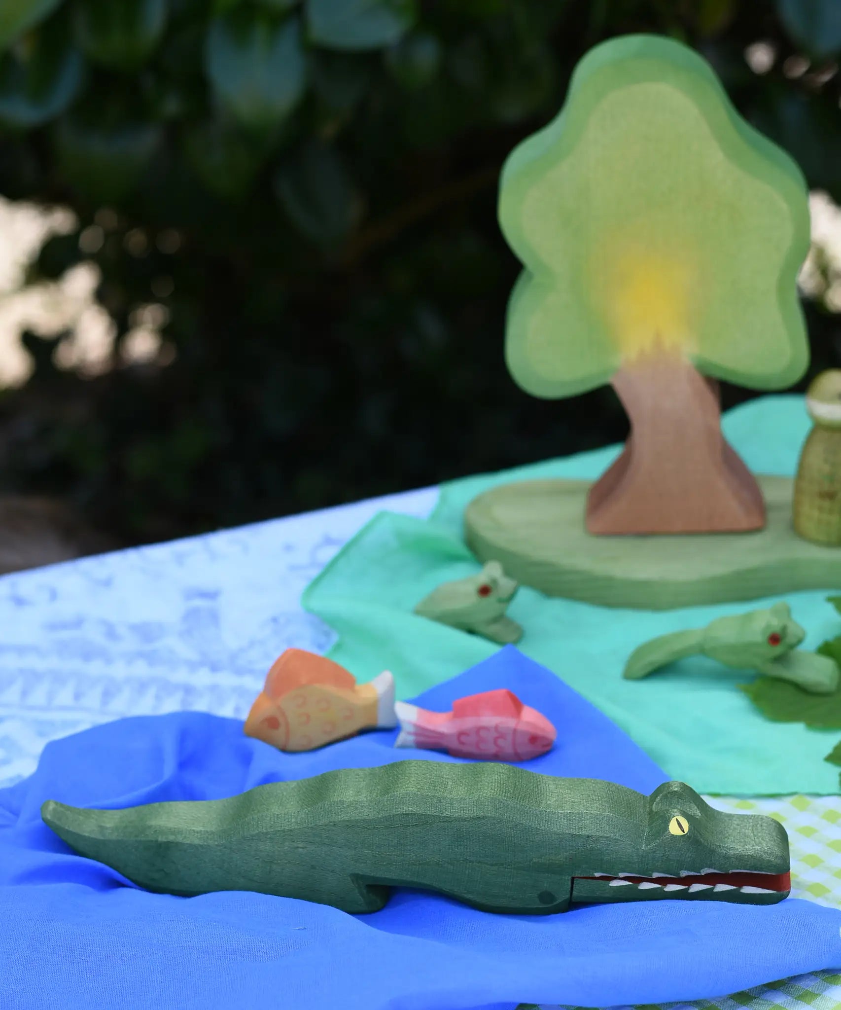 Ostheimer crocodile wooden toy figure placed on a blue Laura's cotton play cloth in a small world play scene. 