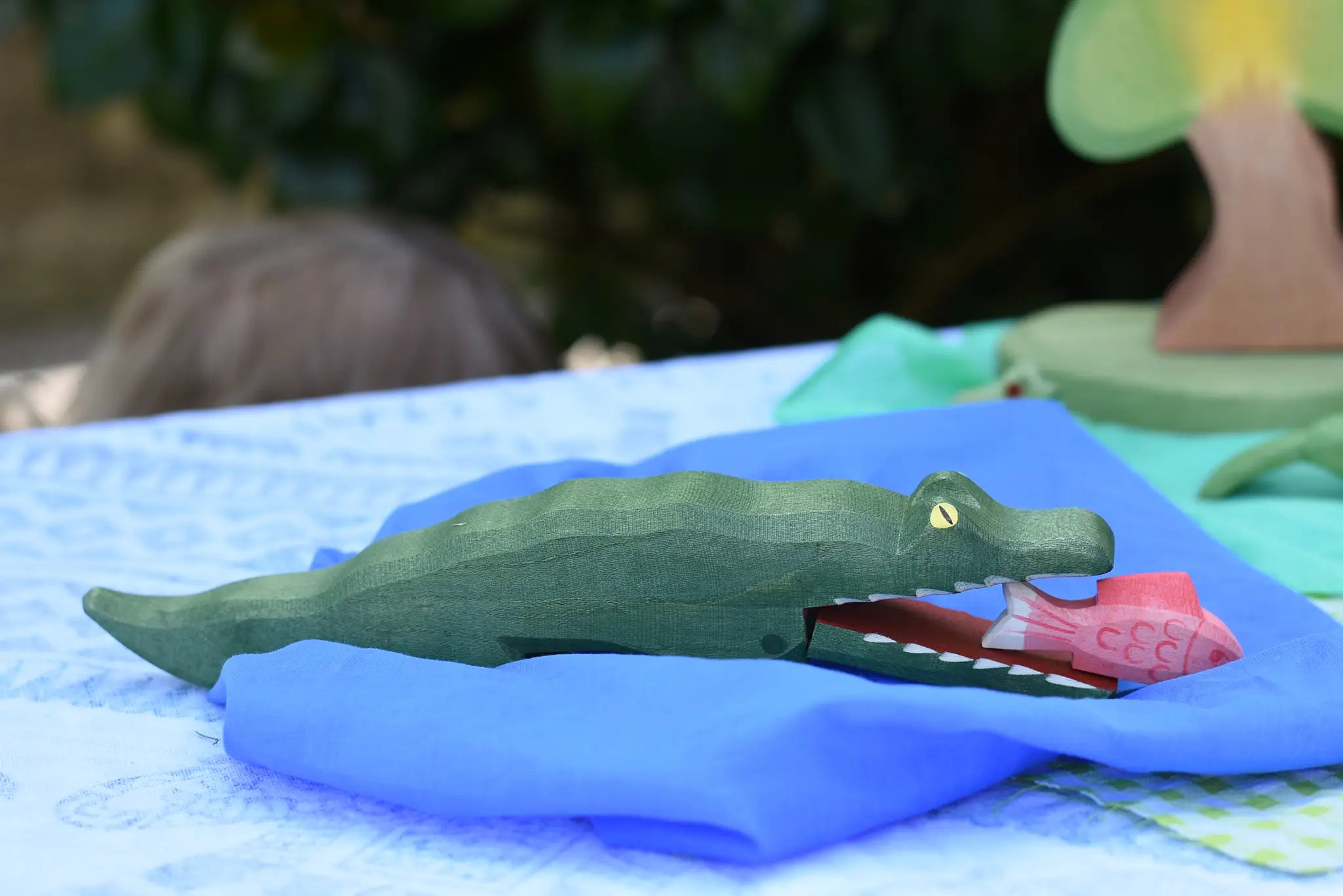 Ostheimer crocodile wooden toy figure on a blue Laura's play cloth. Red fish has been placed in the crocodiles mouth. 