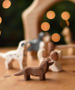 An Ostheimer Dachshund dog wooden toy figure placed at the front of a small world play scene with other dog figures in the background.  These wooden figures are part of a wide range of expertly hand crafted wooden toys here at Babipur. 