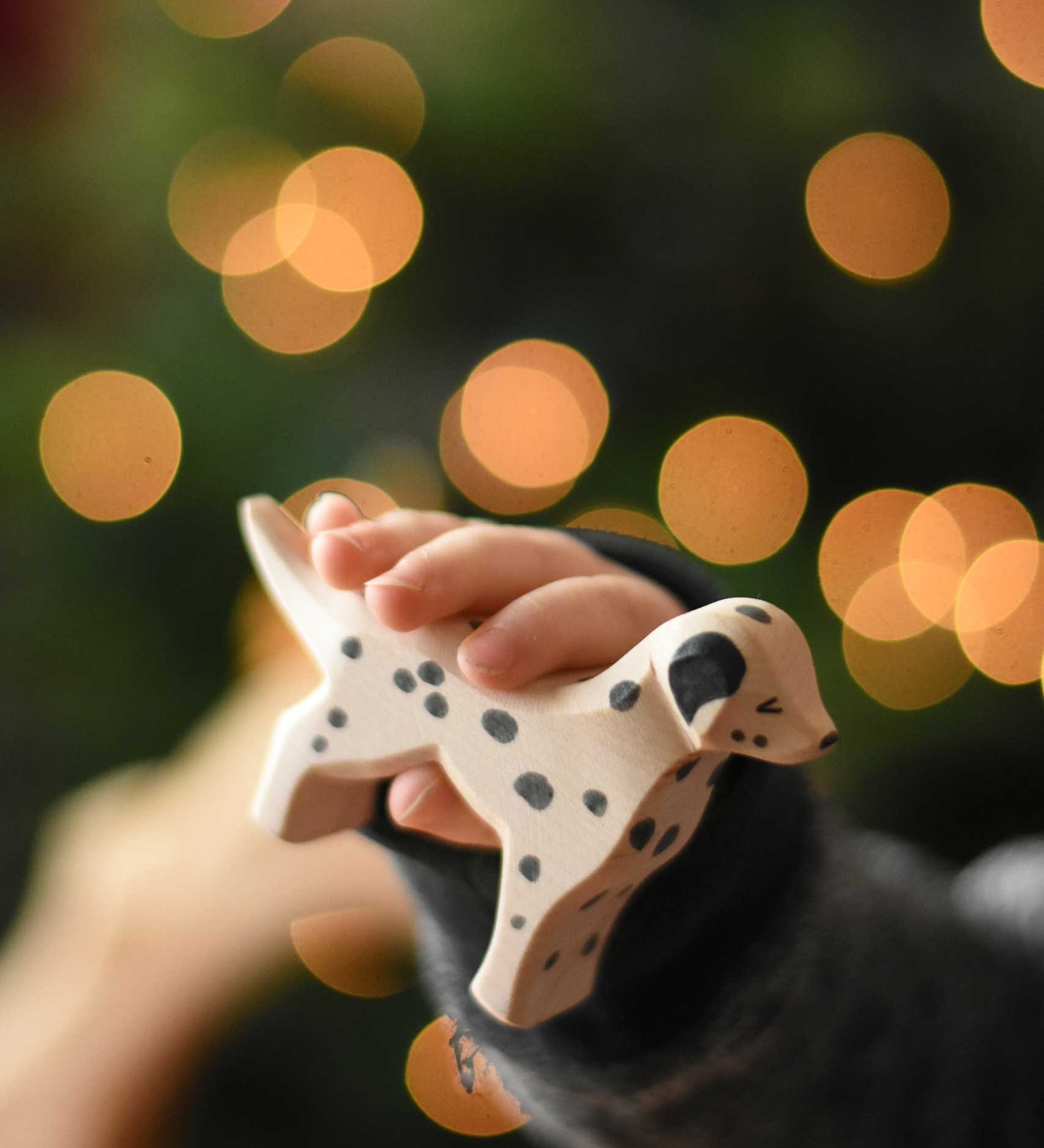 A close up of an Ostheimer dalmatian wooden toy dog figure in a child's hand. These wooden figures are part of a wide range of expertly hand crafted wooden toys here at Babipur. 