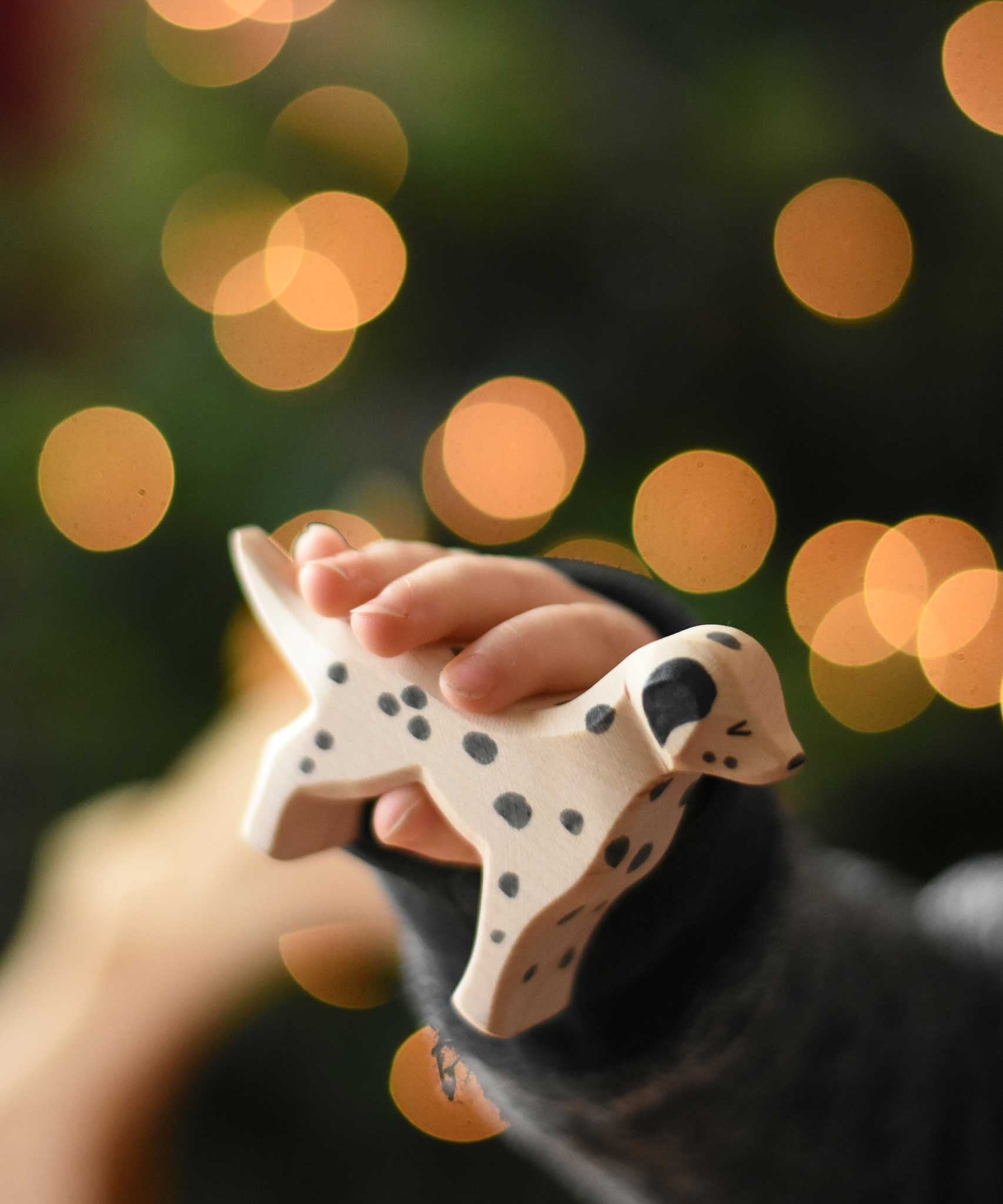A close up of an Ostheimer dalmatian wooden toy dog figure in a child's hand. These wooden figures are part of a wide range of expertly hand crafted wooden toys here at Babipur. 