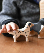 A close up of a child's hand reaching for the Ostheimer dalmatian wooden toy dog figure. These wooden figures are part of a wide range of expertly hand crafted wooden toys here at Babipur. 