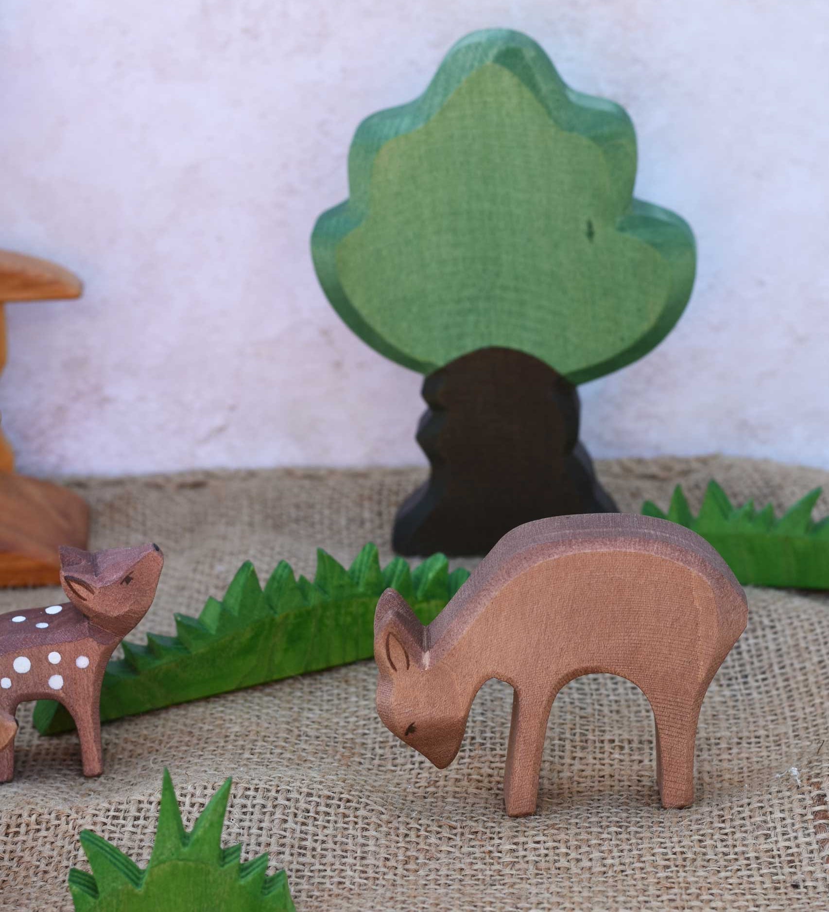 An Ostheimer eating deer wooden toy figure placed in a small world play scene with other fawn and deer and Ostheimer grass and an oak tree. Check out our full range of expertly crafted wooden toy figures and scenery here at Babipur.
