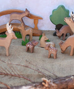 A collection of Ostheimer deer and fawn wooden figures placed in a small world play scene set up with a wooden toy bridge, oak tree and green grass figures. Check out our full range of expertly crafted wooden toy figures and scenery here at Babipur.