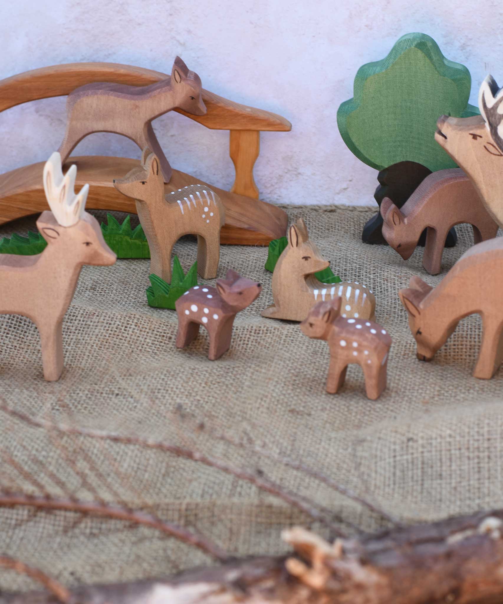 A collection of Ostheimer deer and fawn wooden figures placed in a small world play scene set up with a wooden toy bridge, oak tree and green grass figures. Check out our full range of expertly crafted wooden toy figures and scenery here at Babipur.