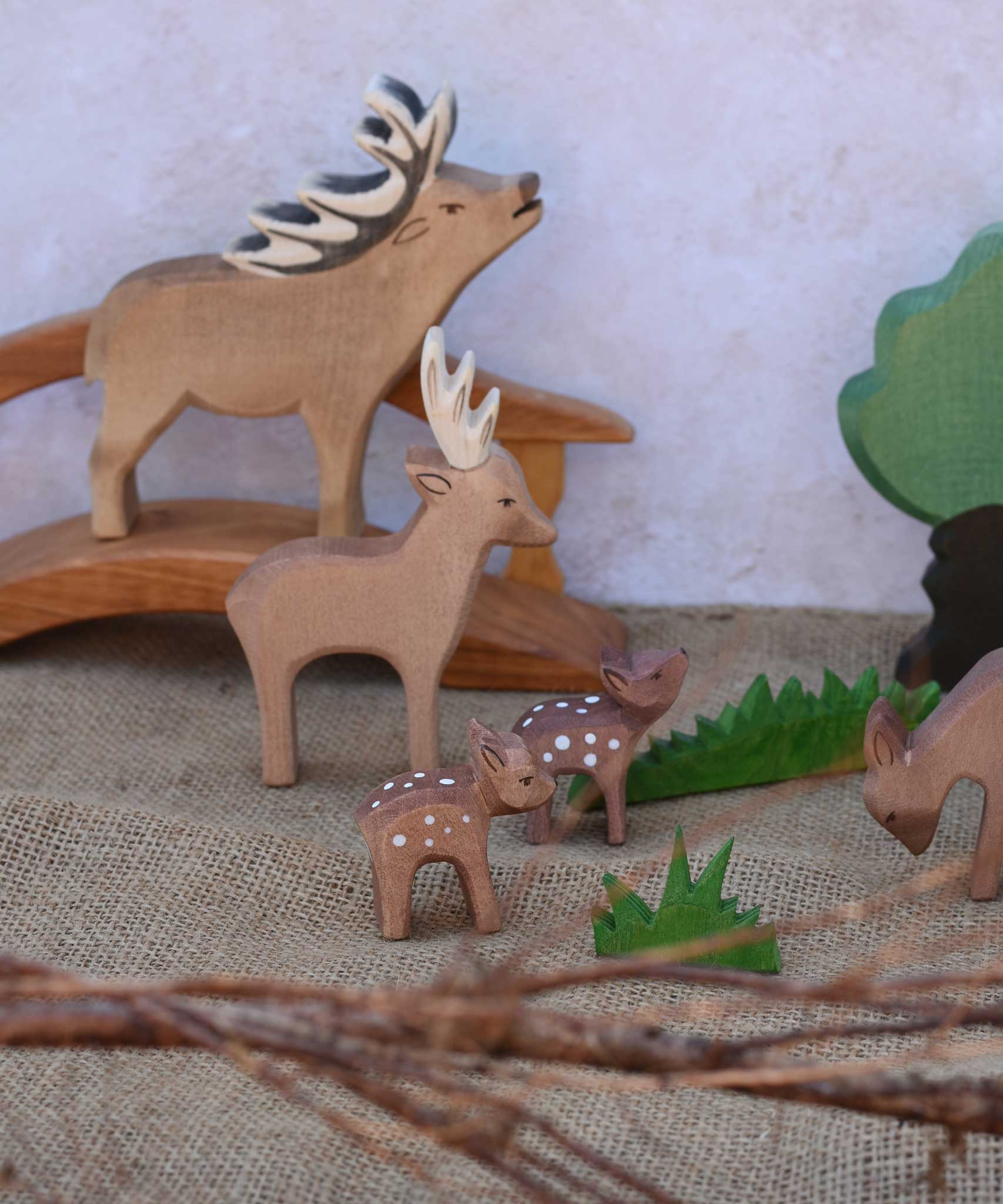 A collection of Ostheimer deer and fawn shown in a small world play scene with a wooden toy bridge and trees and branches. Check out our full range of expertly crafted wooden toy figures and scenery here at Babipur.