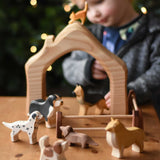 A collection of Ostheimer Dogs wooden toy figures placed in a small world play scene with a house shaped block piece and wooden toy fences.  These wooden figures are part of a wide range of expertly hand crafted wooden toys here at Babipur. 