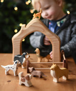 A collection of Ostheimer Dogs wooden toy figures placed in a small world play scene with a house shaped block piece and wooden toy fences.  These wooden figures are part of a wide range of expertly hand crafted wooden toys here at Babipur. 