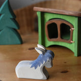 Ostheimer donkey laying down wooden toy figure placed in a simple small world play scene with a small spruce tree in the background and a green hutch. 
