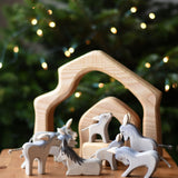 A collection of Ostheimer wooden donkeys handmade figures placed on  a wooden surface. The Ostheimer 4 piece house set can be seen in the background. Ostheimer's range of hand crafted, heirloom quality wooden toys are available to buy at Babipur. 