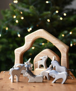 A collection of Ostheimer wooden donkeys handmade figures placed on  a wooden surface. The Ostheimer 4 piece house set can be seen in the background. Ostheimer's range of hand crafted, heirloom quality wooden toys are available to buy at Babipur. 