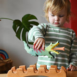 Ostheimer green dragon handmade wooden toy figure in a child's hand hovering above the castle bridge. 