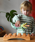 Ostheimer green dragon handmade wooden toy figure in a child's hand hovering above the castle bridge. 