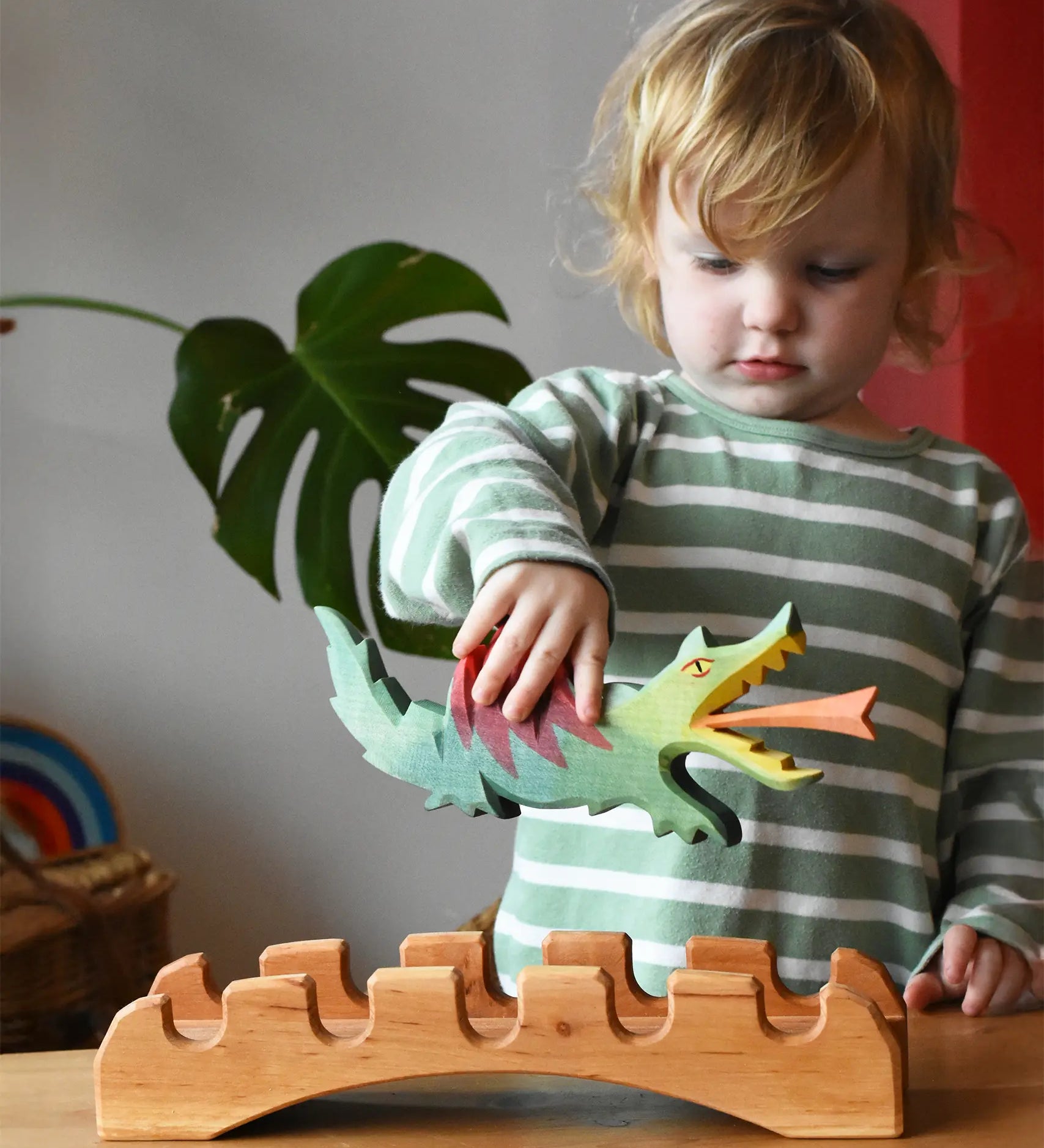 Ostheimer green dragon handmade wooden toy figure in a child's hand hovering above the castle bridge. 