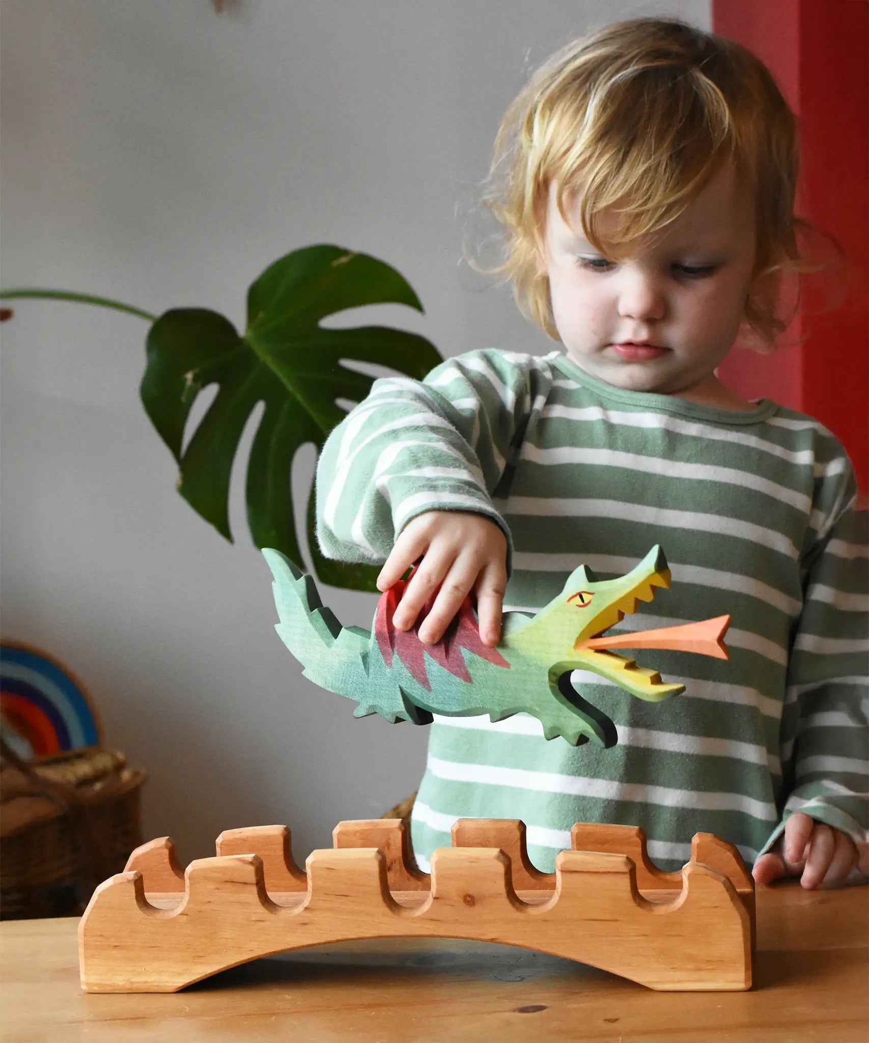 Ostheimer green dragon handmade wooden toy figure in a child's hand hovering above the castle bridge. 