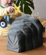 Back of the black Ostheimer dragon's cave, a child is placing a yellow wooden star decoration on top.