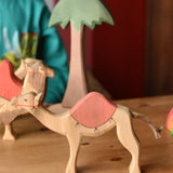 Ostheimer dromedary camel figure with saddle placed in a small world play set up with other camels and a tall palm tree in the background.