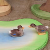 Two Ostheimer wooden ducks placed on a wooden pond scene piece. One duck is in a swimming position one is standing and has a long neck position.